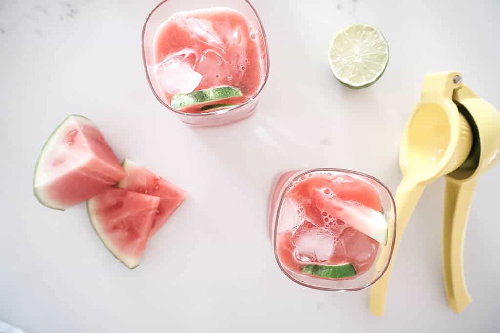 Flat lay of super simple watermelon margarita's with limes and juicer in the background