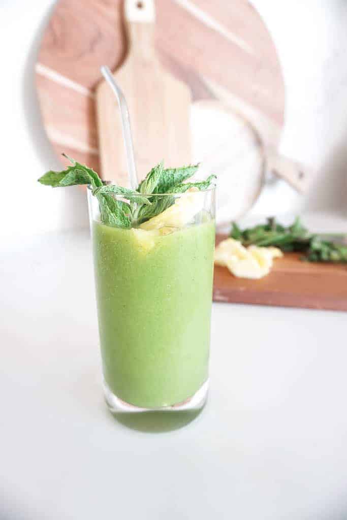 Image of a refreshing smoothie - with pineapple and mint sticking out of the glass with the green smoothie. Plus more pineapple and mint in the background.