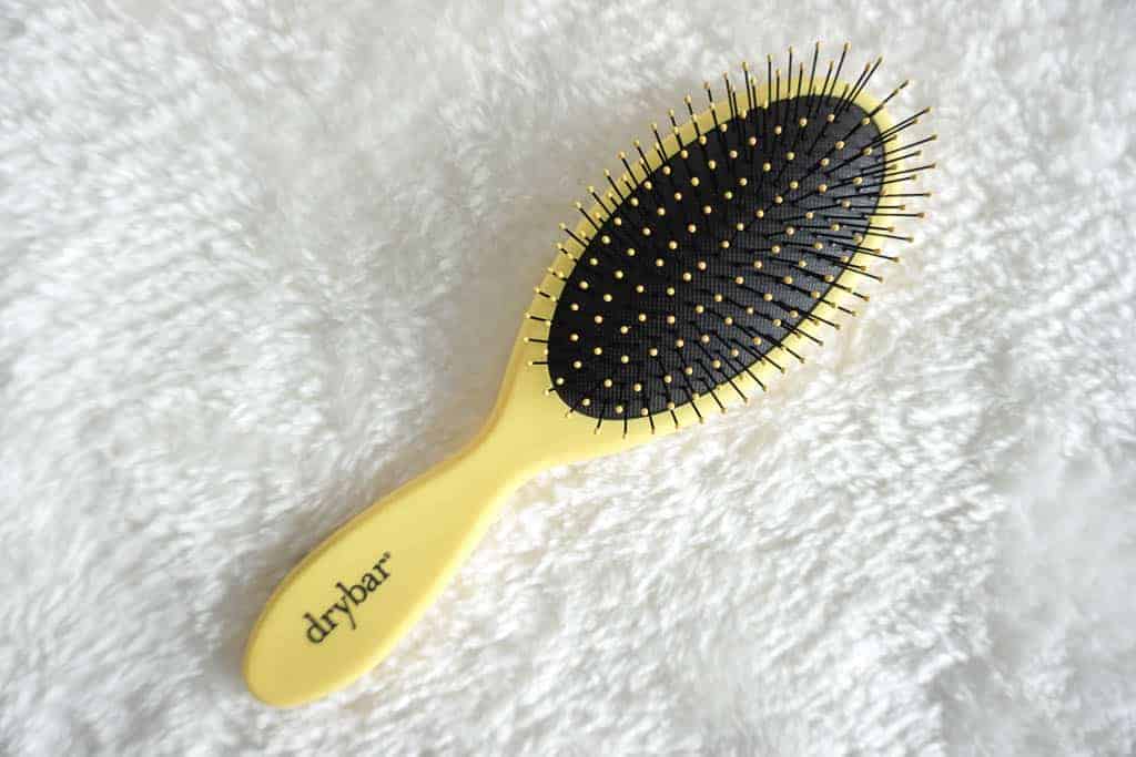 yellow dry bar hair brush laying flat on a fuzzy blanket
