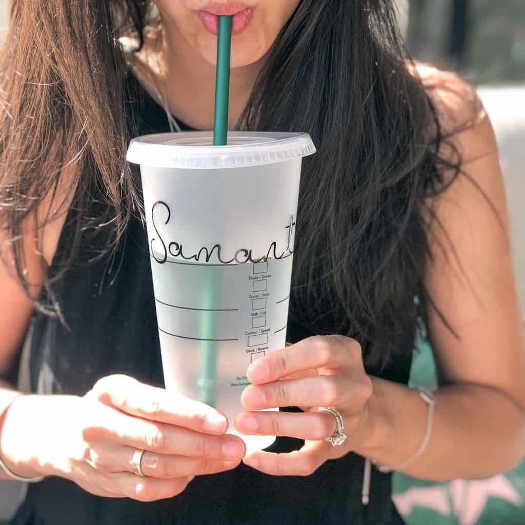 Signed Samantha's Nifty Gifty Post Ideas - this one is an image of Samantha holding up a faux, clear, plastic, Starbucks cup with her name written on it in cursive. She is taking a sip from the straw.