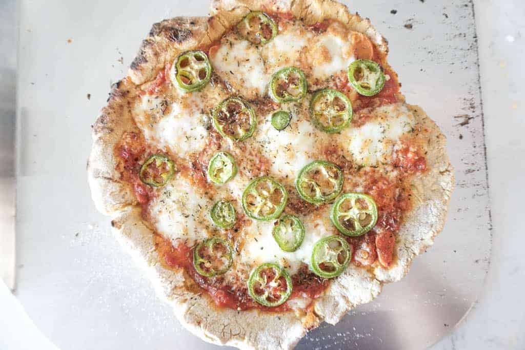 Signed Samantha's recipe for gluten free pizza crust - the cooked crust is pictured with jalapenos on a cheese pizza