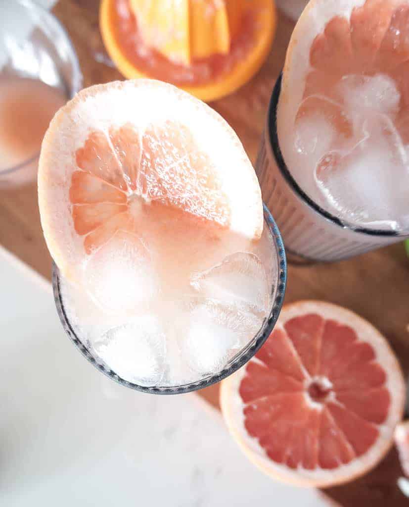 Signed Samantha's easy paloma recipe - two completed palomas are pictured with grapefruit rounds sliced into them and ice sticking out. You can see grapefruit slices and halves in the background.