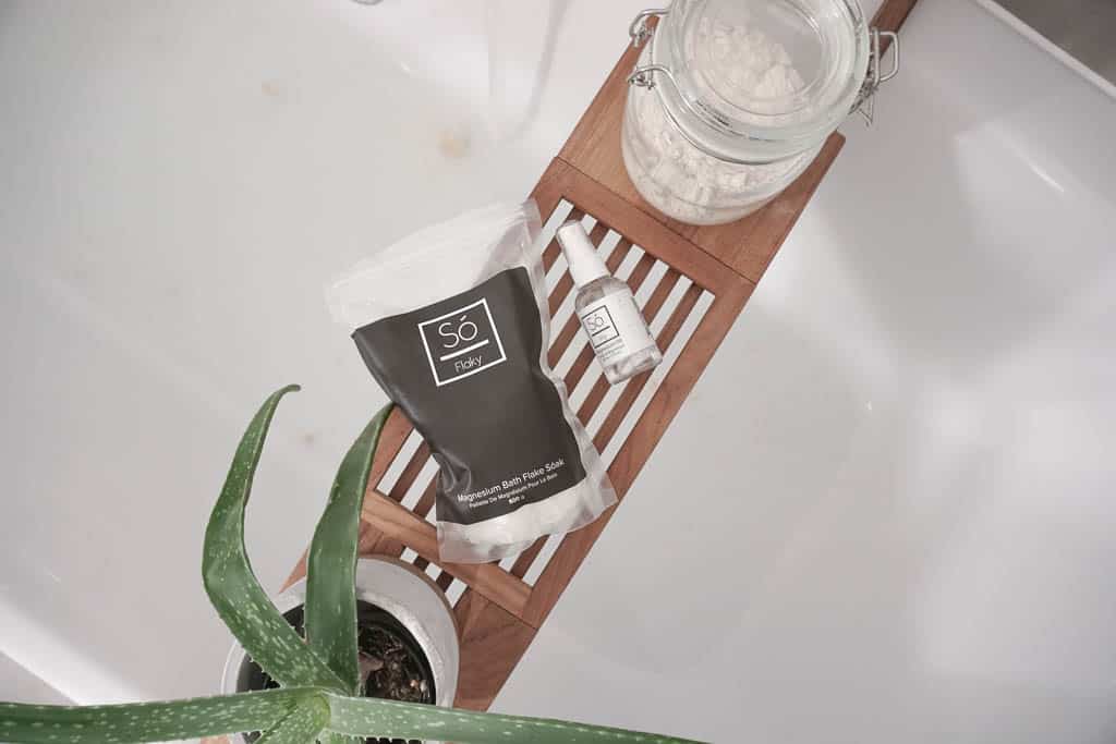 September's Local Love features includes SO Luxury - their magnesium flakes, spray, and coco oat bath is on top of a bath caddy with a running bath in the background