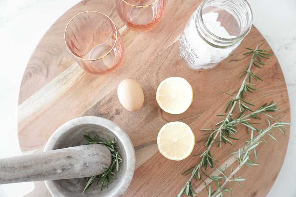 Signed Samantha's bourbon sour ingredients are out on a big round cutting board including lemons, eggs, rosemary.