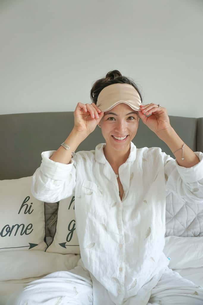 Signed Samantha talking about her bedtime necessities including a silk eyemask pictured on her head, and linen pjs, which she is wearing while sitting cross legged on her bed