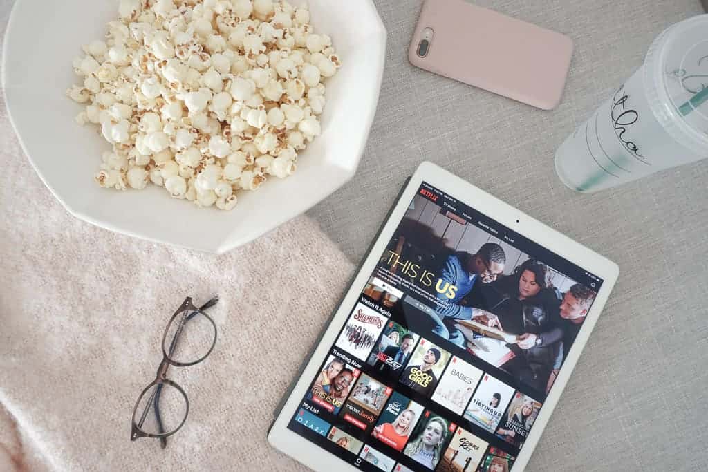 Best shows to watch on netflix now - netflix is on the ipad, with a bowl of popcorn, glasses, water, and iphone pictured on a blanket