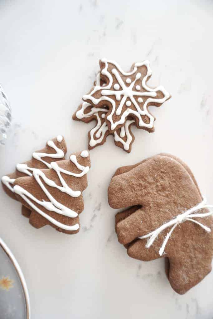 Gluten free gingerbread cookies are pictured with white icing on a marble counter. There are trees, snowflakes, and bears