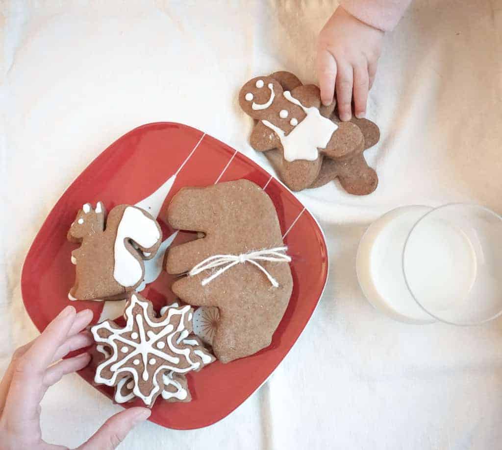 How to Make your home feel more festive includes baking goods like these gingerbread men, bears, squirrels, and snowflakes pictured on a red plate with Signed Samantha and her daughter's hands each reaching for one.