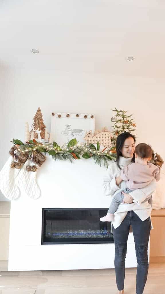 The 2020 Holiday Gift Guide Round Up is ready to go. Signed Samantha is holding her daughter in front of her festively decorated holiday mantle