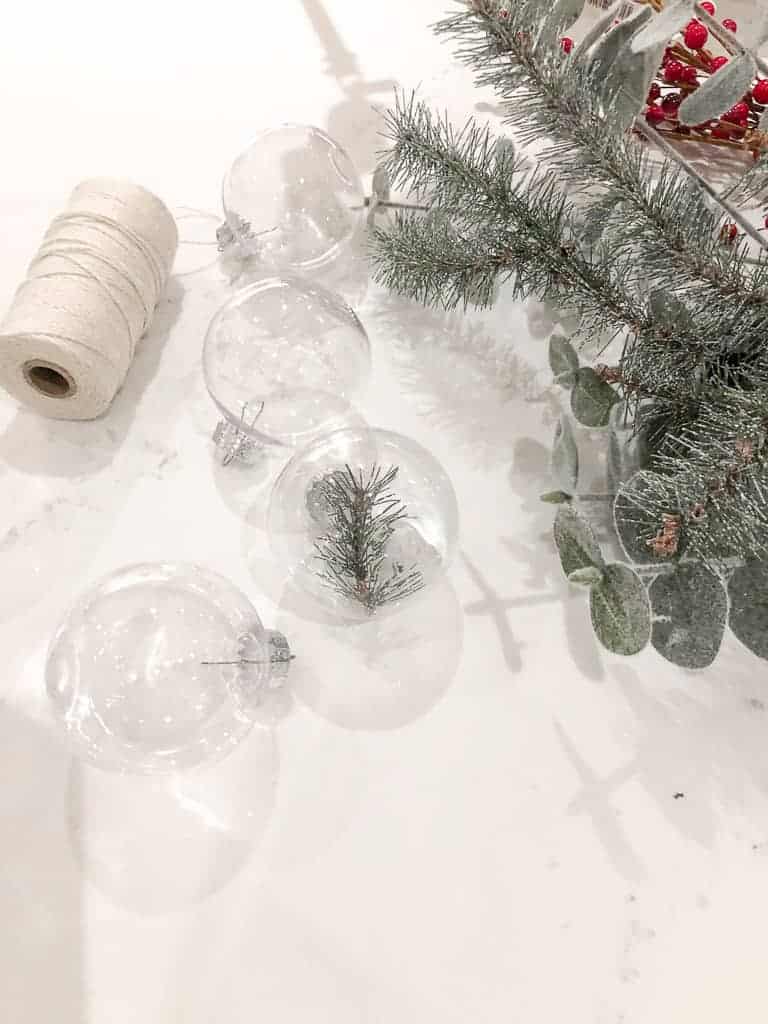 The materials needed to make D.I.Y Christmas Ornaments with Greenery including plastic ornaments, faux greens, and twine