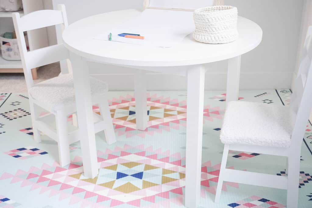 D.I.Y Kids Chair Cushion on top of white chairs and sitting next to a round table. The cushion is white boucle fabric.