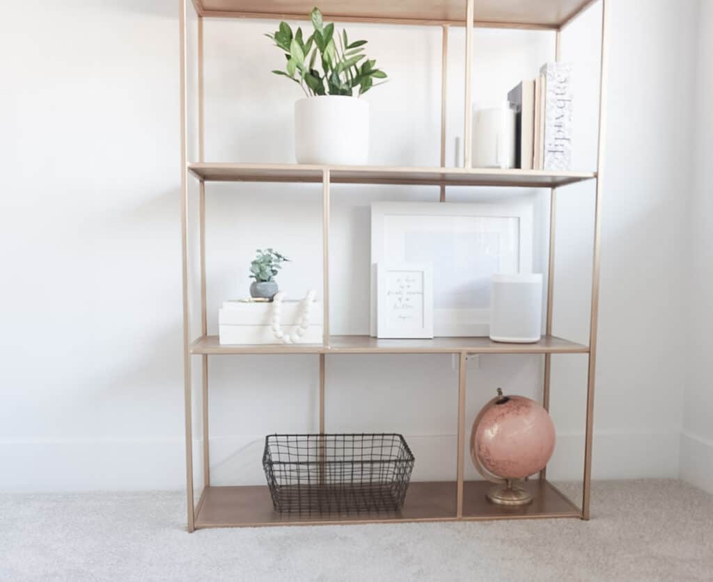 Sharing how to style shelves - showing the completed version on a gold shelf that has books, plants, pictures, and a globe.