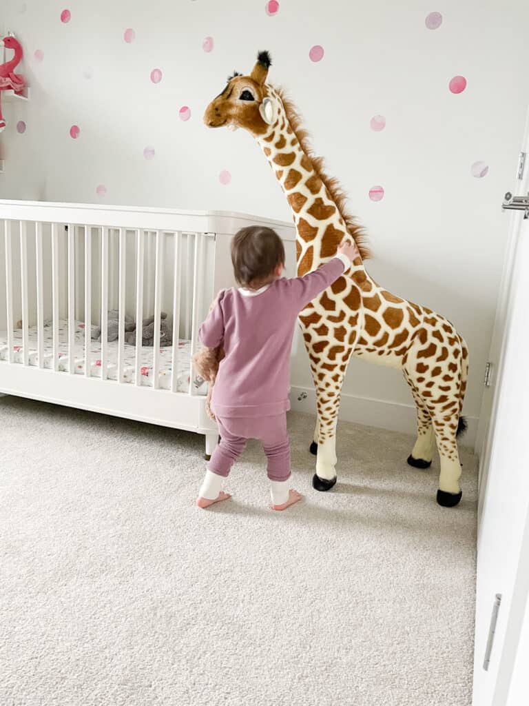 Highlighting local Vancouver shops including Brighton handmade which is where this purple lounge set that Sloane is wearing is from. She is wearing it in her room where the crib and a gigantic giraffe are pictured and she is petting the giraffe.