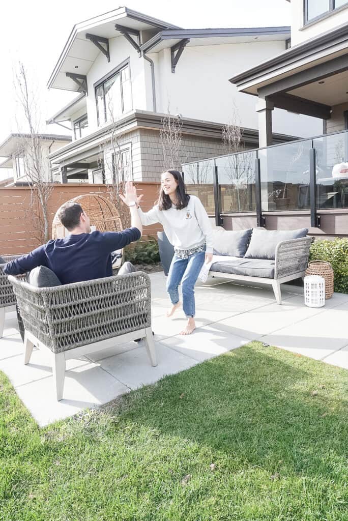Signed Samantha high-fiving her husband on top of their freshly installed patio paving stones. her husband is sitting in one of the patio chairs and Samantha is standing.
