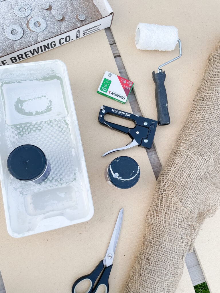The materials you need for a DIY push pin board including scissors, particle board, paint, staple gun.