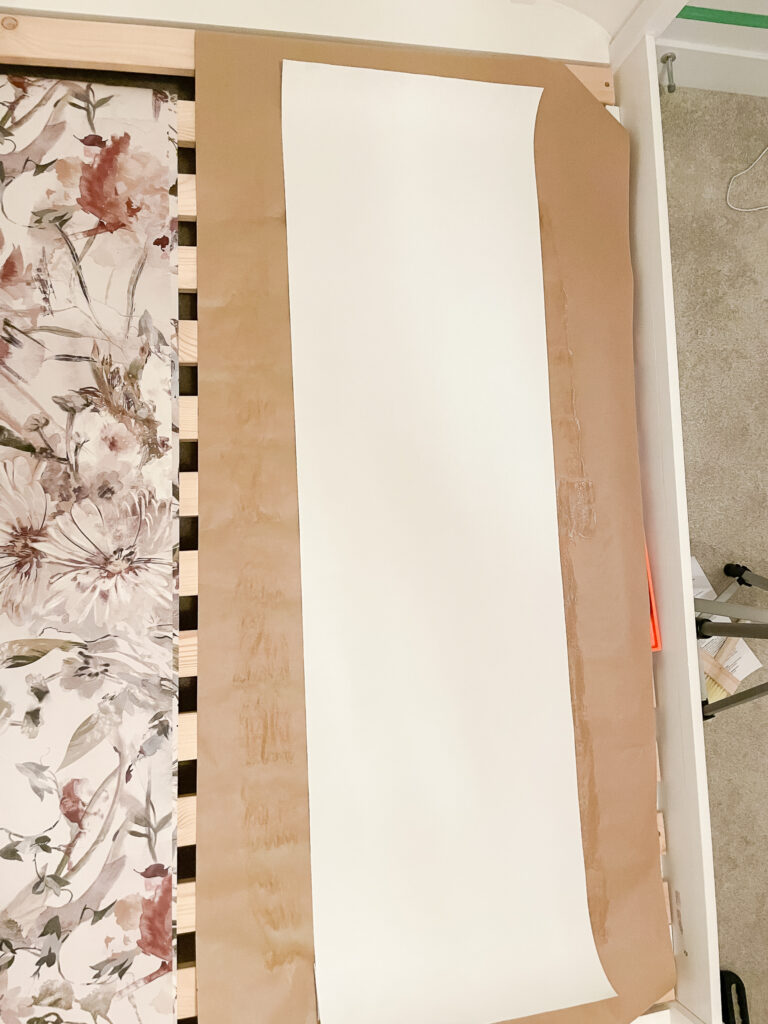 learning about installing glue-based wallpaper with wallpaper on half of a wall. the wallpaper is a beautiful floral print with creams, magentas, and blue hues - there is another piece lying flat on craft paper waiting for glue.