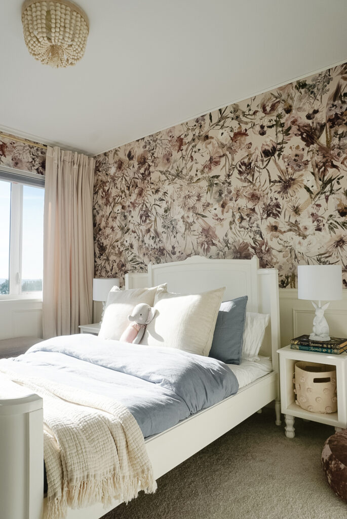 things to consider when costing a DIY project - A big girl room with floral wallpaper, chair rail, box moulding, a white bed frame, blue duvet cover, end tables, and a pouf on the ground
