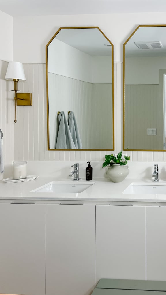 builder grade bathroom gets an upgrade with two gold mirrors, gold sconces, beadboard on the walls with a creamy white.