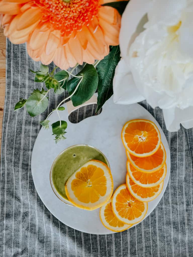 green smoothie, a bunch of sliced orange, and beautiful flowers