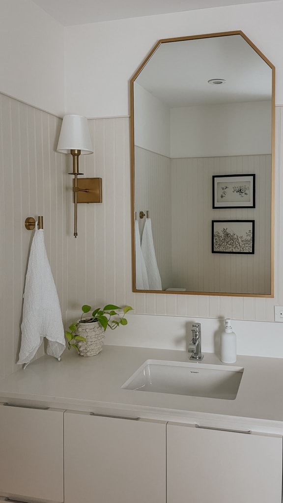 A bathroom pictured with art, a big mirror from a Canadian home decor store, towels, and a sconce
