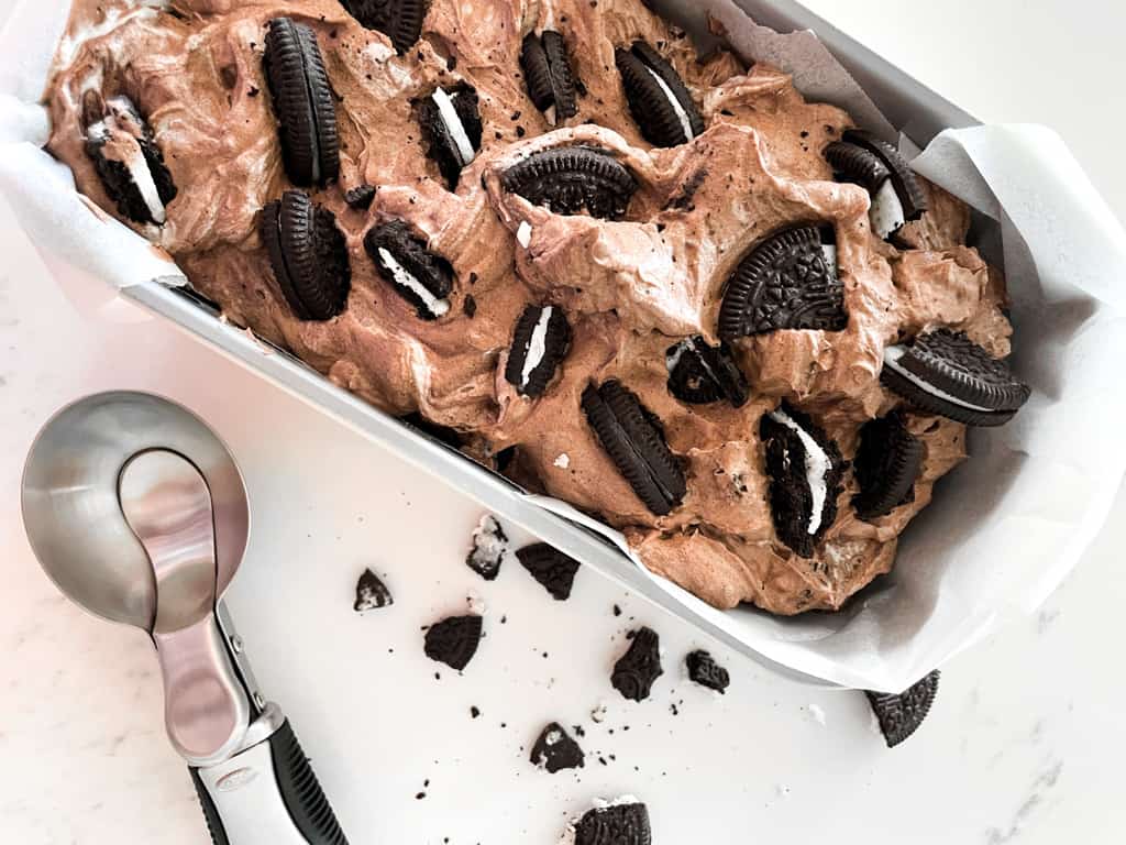 chocolate oreo ice cream pictured in a loaf pan with an ice cream scoop next to it