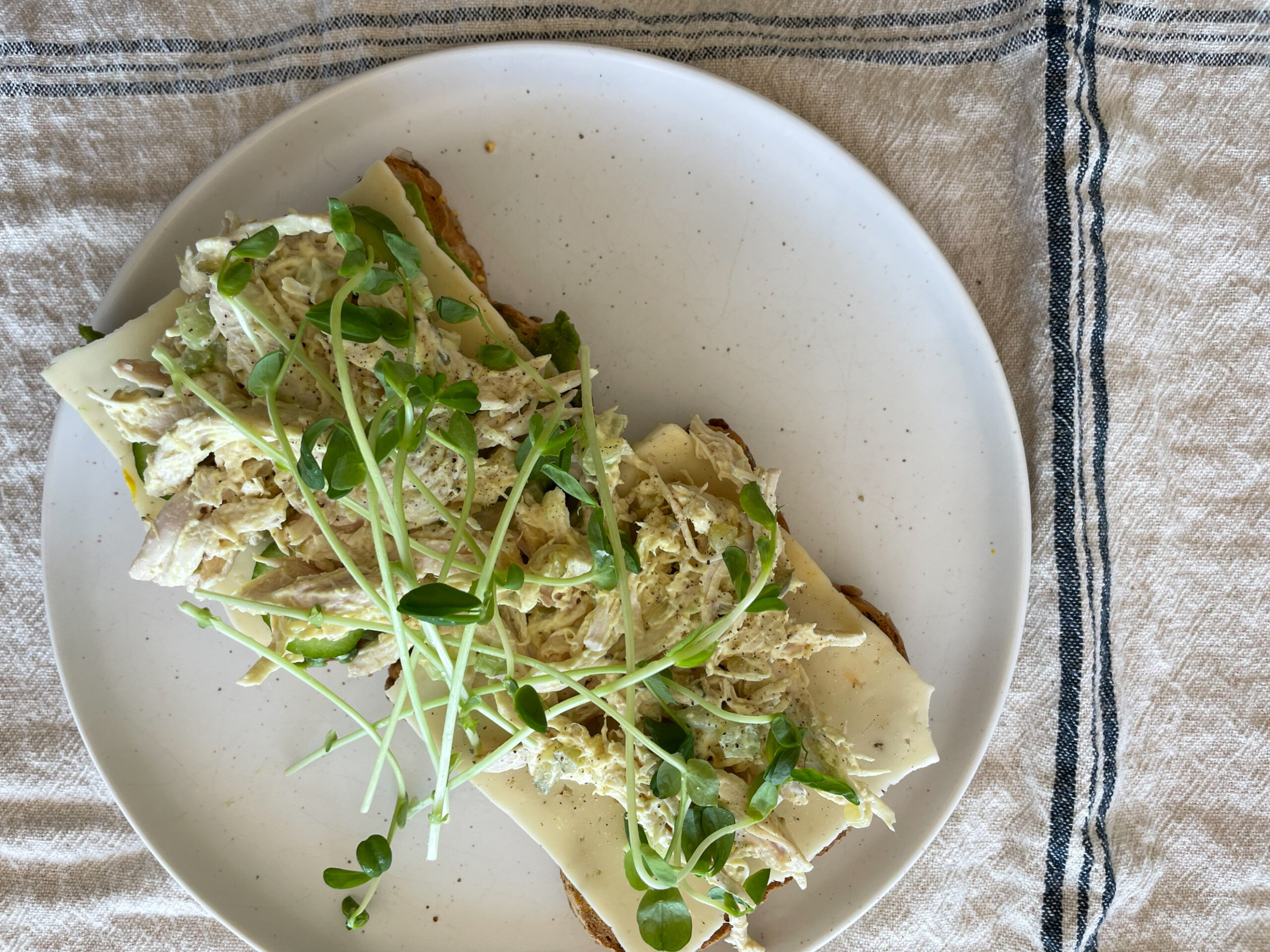 chicken salad sandwich on a plate with microgreens on it