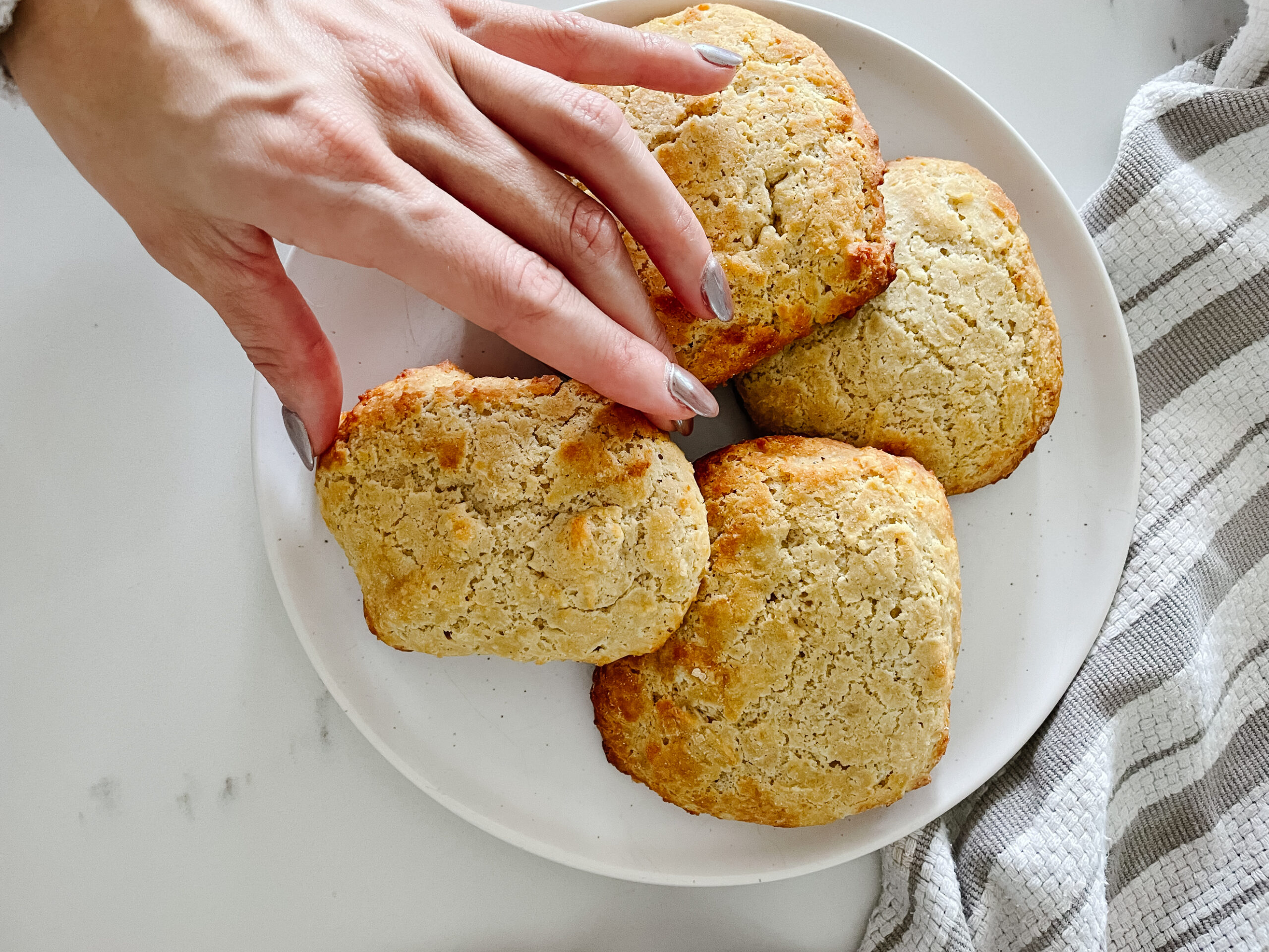 gluten-free biscuits on a plate. one is being picked up by a hand