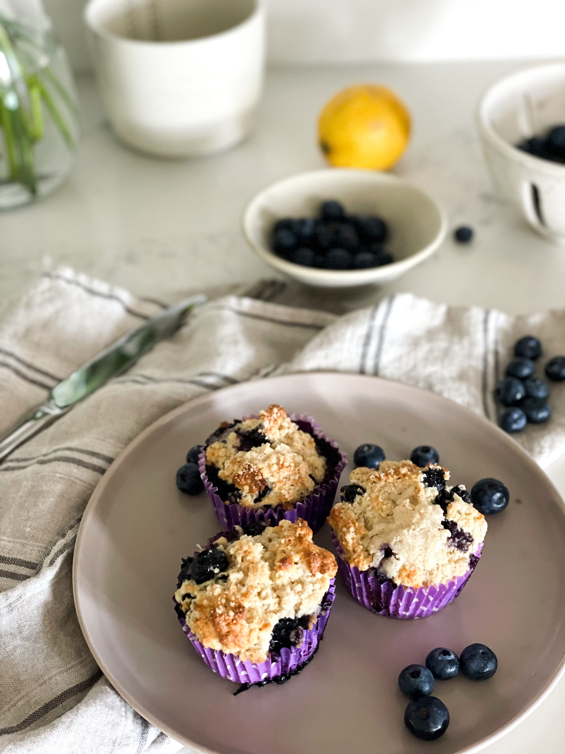 gluten-free blueberry lemon muffins on a plate in the foreground