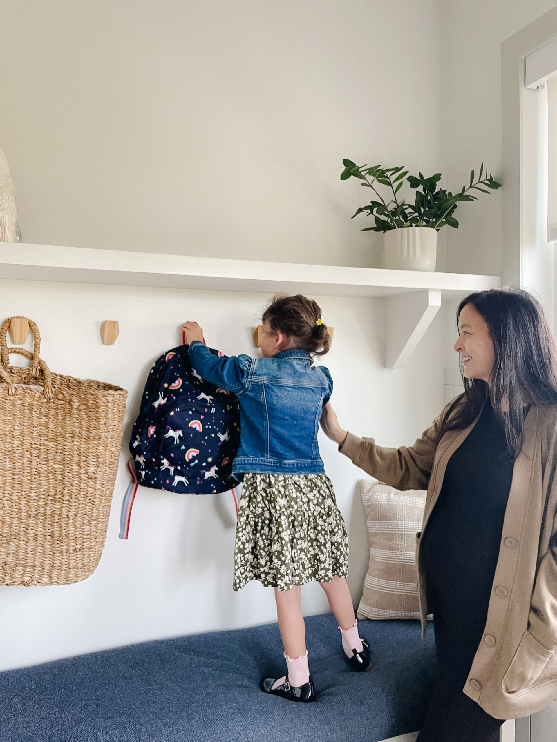 Mom helping little girl get her backpack and her back-to-school outfit ready in the mudroom