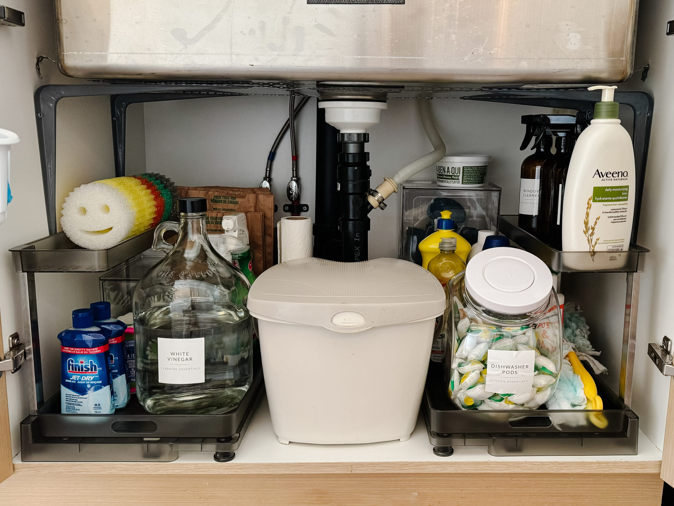 under the kitchen sink organization with a pull out drawer, glass container for vinegar, scrub daddys and more cleaning supplies