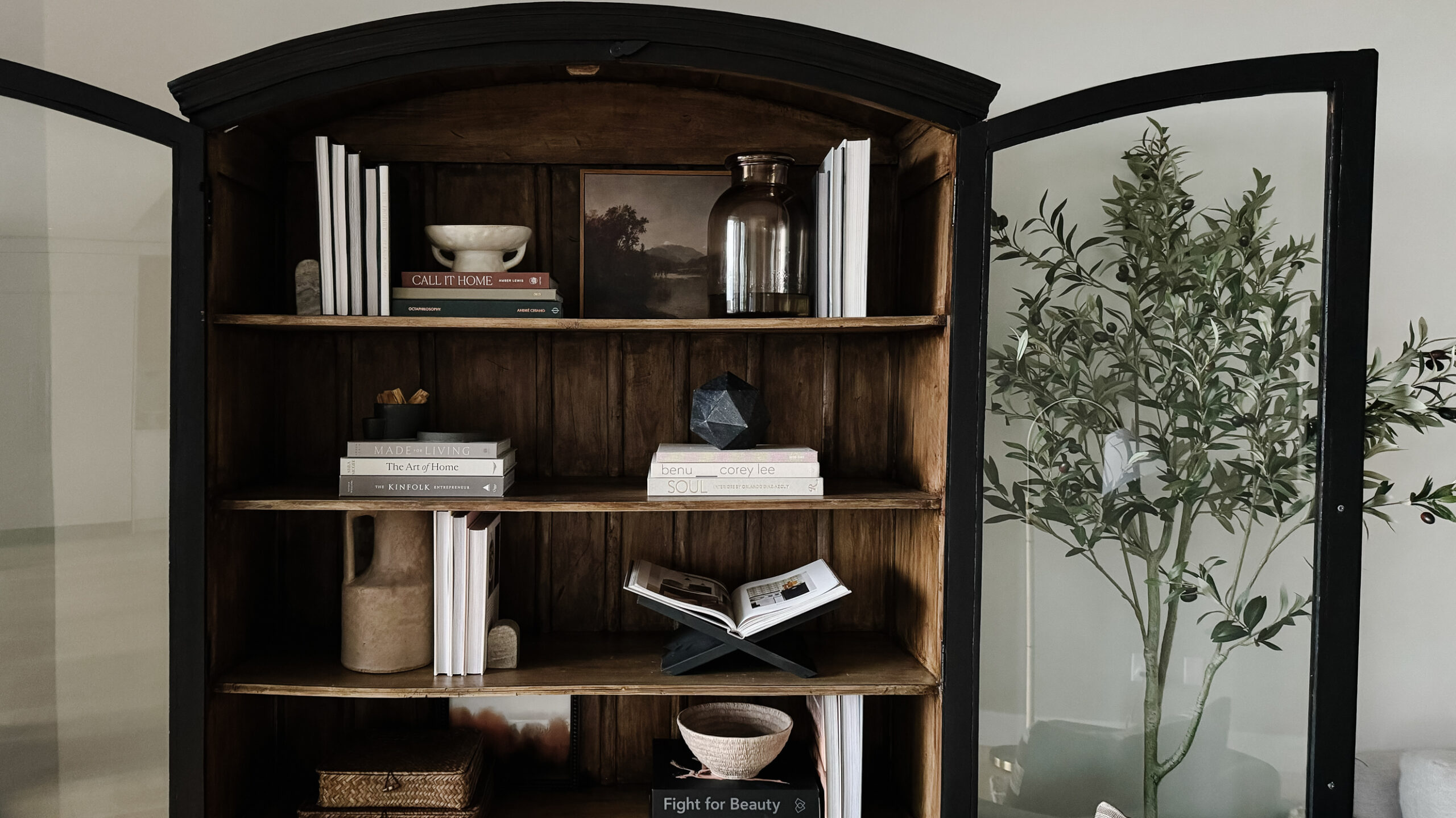 Styling Shelves - a black bookshelf cabinet that is arched with wood interior having been styled with vases, pots, books, etc. is on display